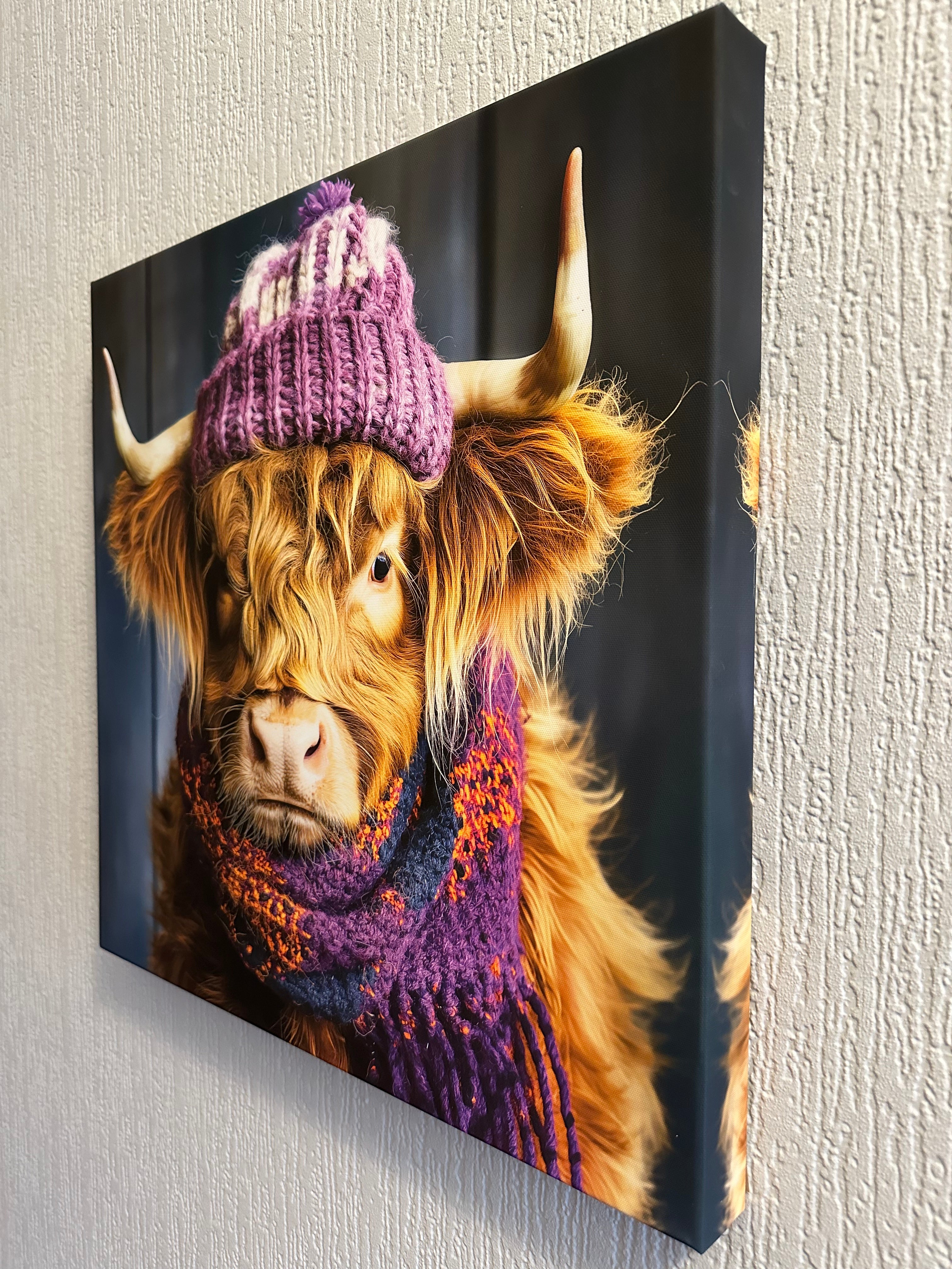 Canvas print of a Highland cow wearing a knitted hat on a textured wall.
