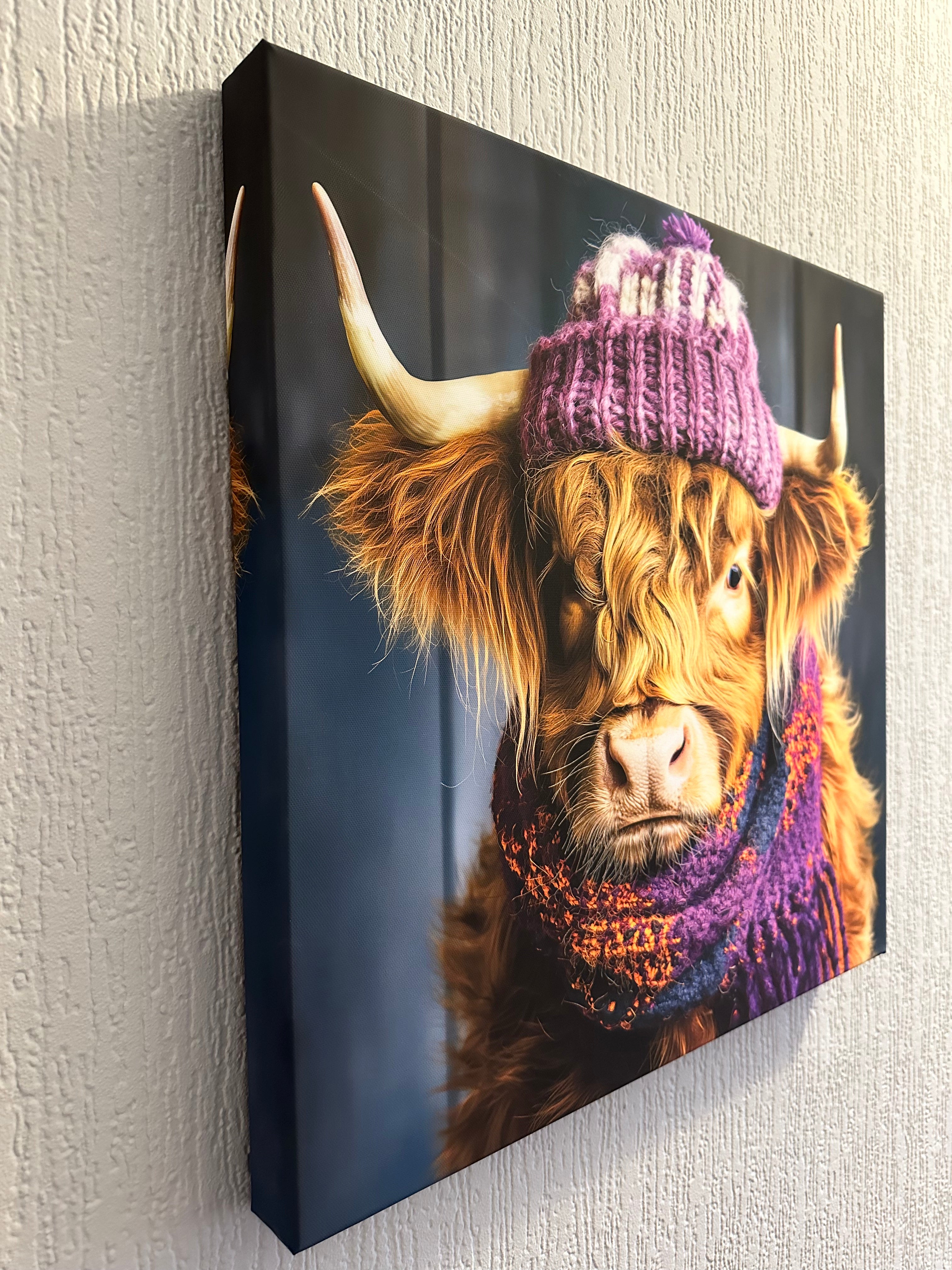 Canvas print of a highland cow wearing a knitted hat on a textured surface