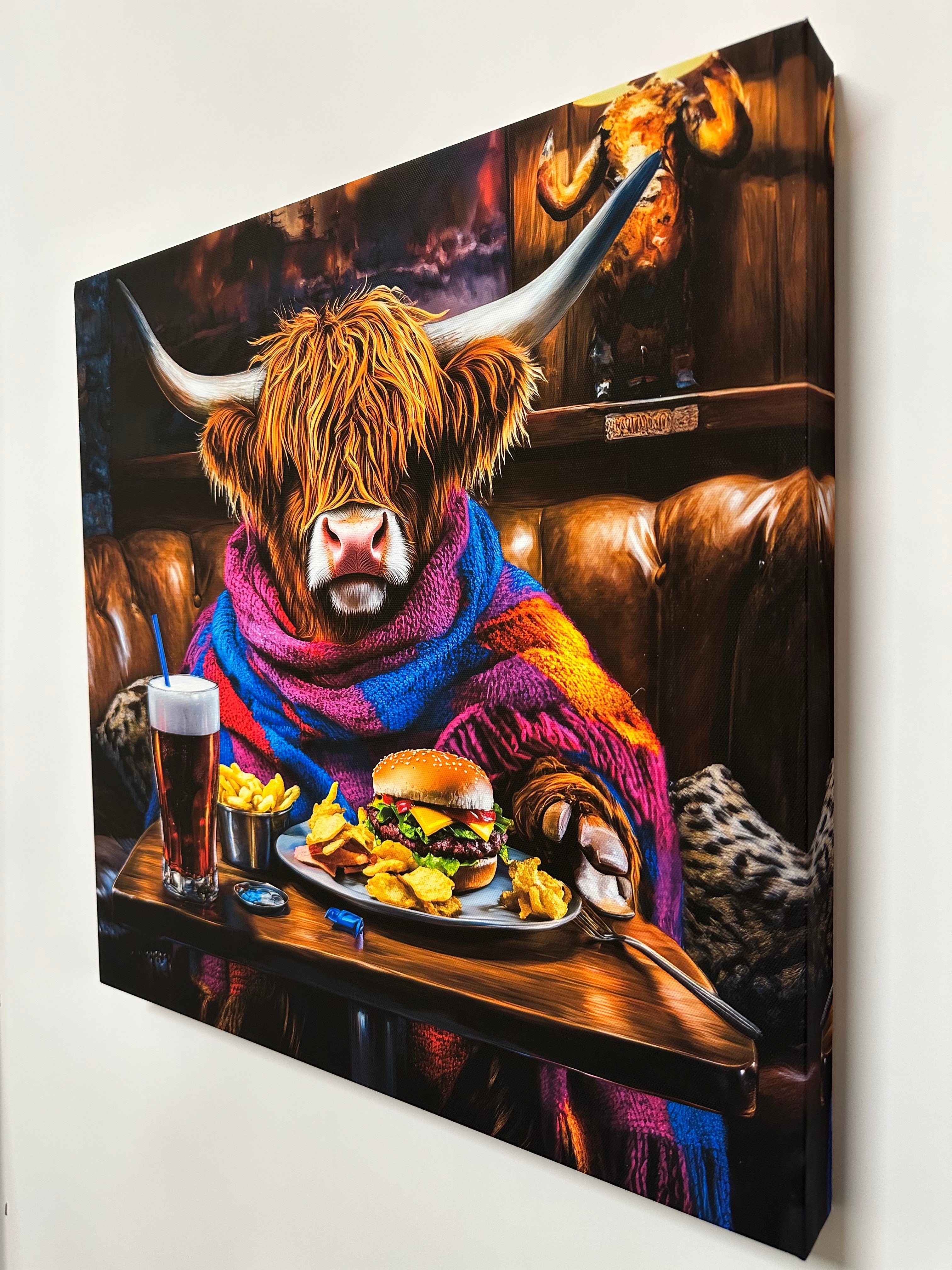 Canvas print of a cow wearing a colorful sweater at a table with food and drinks.