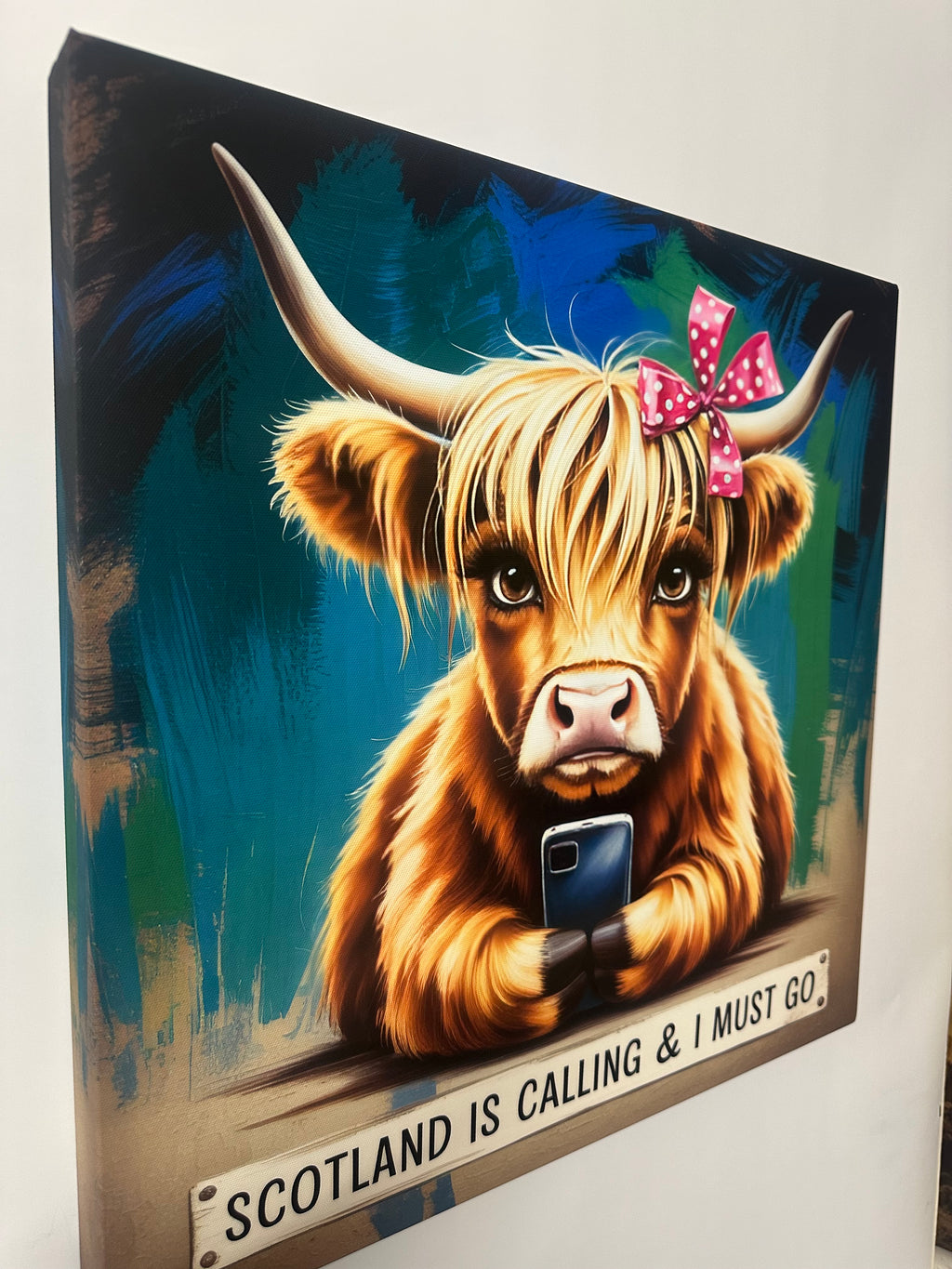 Framed artwork of a highland cow with a bow and 'Scotland is Calling' text.