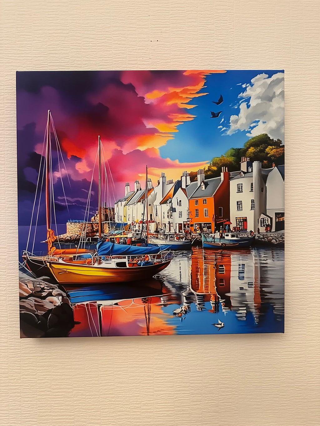 Art print of a harbor scene with houses and boats on a beige wall.