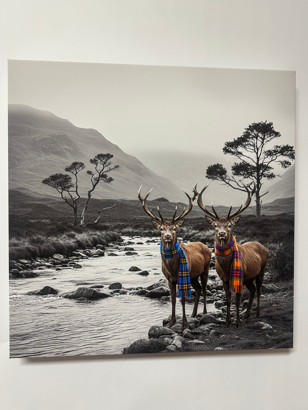 Framed artwork of two deer crossing a river with a mountainous background.