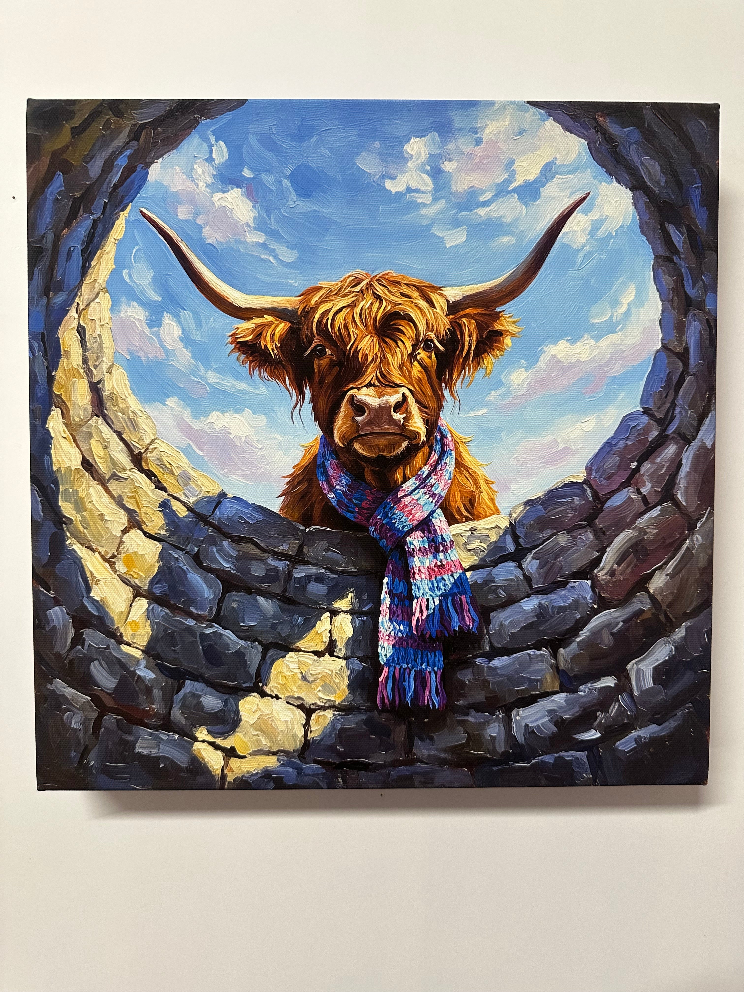 Canvas print  of a highland cow wearing a colourful scarf peering through a stone Water well.