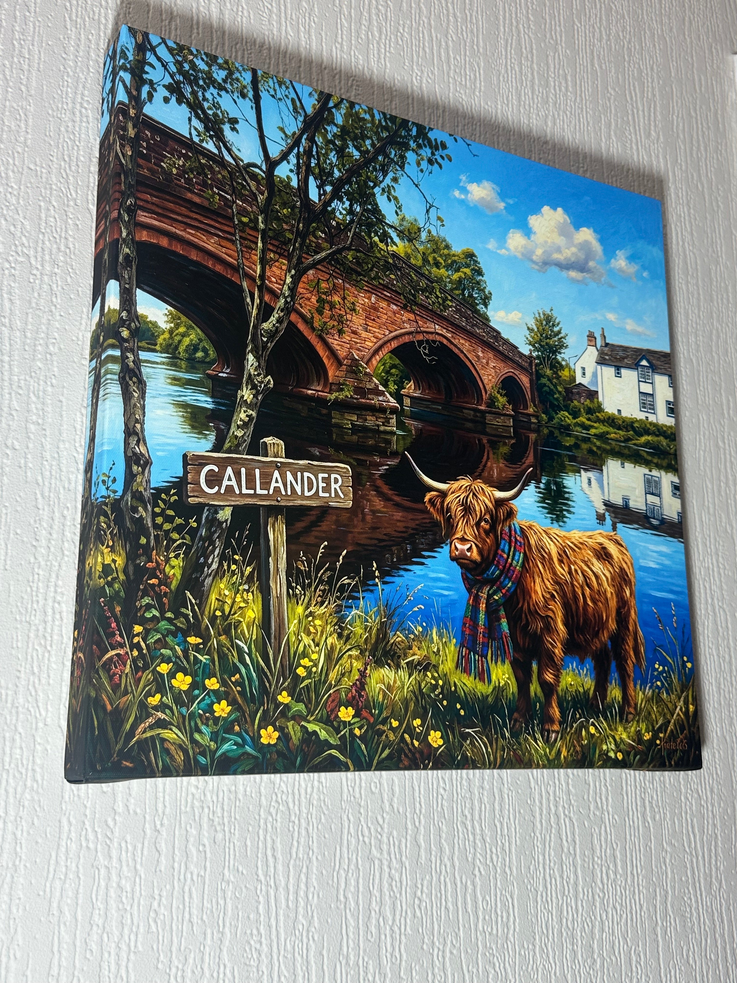 A square canvas print featuring a whimsical illustration of a Highland cow wearing a plaid kilt standing by a bridge with the sign 'CALLANDER', displayed on a textured white wall.