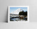 Framed photograph of a deer by a lake with a mountain in the background on a gray wall.